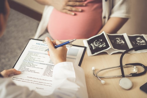Pregnant Woman With Doctor Going Over Document